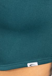Teal geribbelde crop top met een gestructureerde afwerking. Bevat een wit merkvlaggetje aan de zoom. Glad stof met een strakke pasvorm.