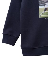 Sudadera azul marino con puños y dobladillo acanalados. Presenta un estampado gráfico en la parte delantera. La tela parece suave, con un acabado texturizado.