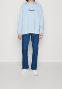 Jasnoniebieska bluza z kapturem z przednią kieszenią i czarną grafiką. Połączona z ciemnoniebieskimi jeansami o prostym kroju i białymi sneakersami. Miękka tkanina, luźny krój.