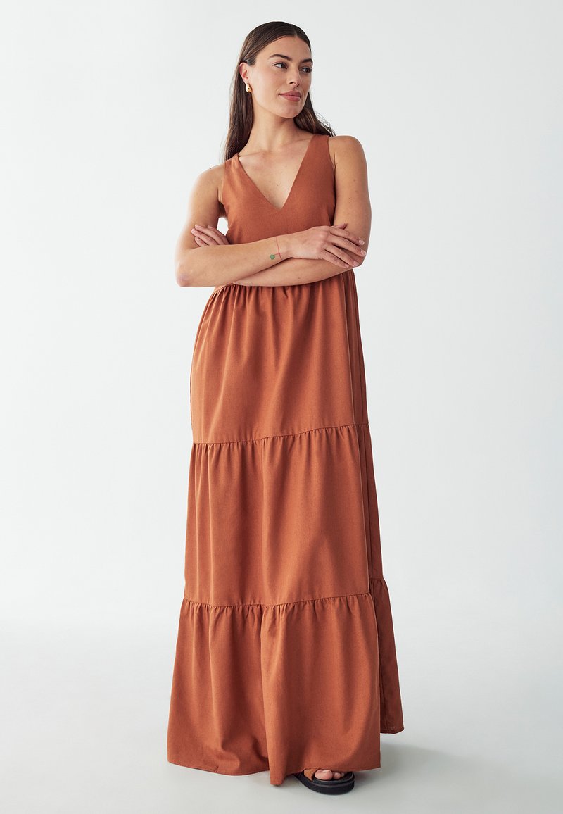 Vestido maxi de color óxido, hecho de una tela suave, con un profundo escote en V, diseño sin mangas y un dobladillo con volantes en capas.