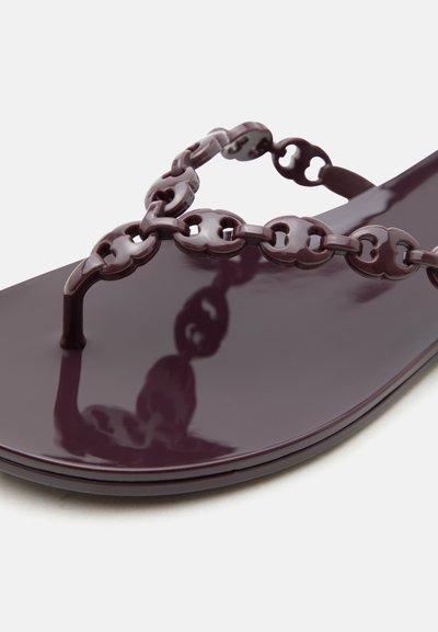 Γυαλιστερό σκούρο μοβ επίπεδο σανδάλι με λουριά με αλυσίδα και λεπτομέρεια ανάμεσα στα δάχτυλα σε λευκό φόντο.