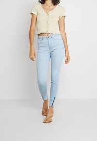 Top corto floral amarillo claro con mangas cortas, combinado con jeans ajustados azul claro que cuentan con cremalleras laterales y un diseño entallado.