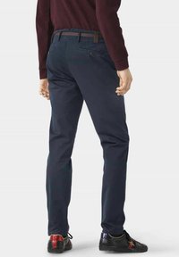 Marineblaue Chinos mit glatter Textur und geradem Schnitt, ausgestattet mit Gesäßtaschen und einem braunen geflochtenen Gürtel. Kombiniert mit schwarzen Sneakers.