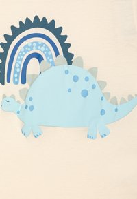 Tela beige claro con un gran gráfico de un dinosaurio plano y azul claro, con manchas azul oscuro y un arco iris azul oscuro detrás.