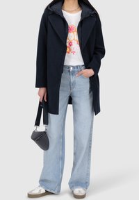 Námořnický kabát s kapucí a zapínáním na knoflíky, doplněný bílým tričkem s potiskem, světlými širokými džíny a béžovými teniskami se šedými detaily.