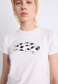 White cotton t-shirt featuring a black and white drawing of a curled rabbit with distinctive spots on its body, located on the front.