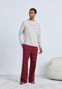 Sweatshirt cinza de algodão com o logótipo "Tommy Hilfiger", combinado com calças de flanela xadrez vermelhas. Textura suave, corte descontraído e punhos canelados.