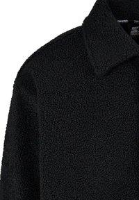 Jachetă din fleece neagră cu un material texturat, guler ascuțit și cusături vizibile. Suprafața are un finisaj moale, pufos.