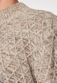 Bežinis megztinis su tekstūriniu deimanto raštu. Medžiaga turi šviesiai rudos, grietinėlės ir tamsesnių siūlų mišinį. Raštuotas apykaklė.