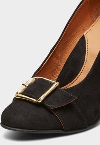 Černé semišové lodičky s oválnou špičkou, ozdobnou mašlí se zlatou sponou a světlým koženým podšívkou.