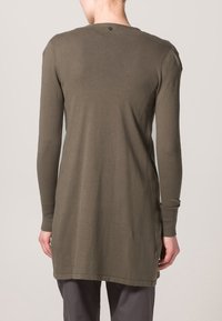 Olivgrön långärmad tunika med rund halsringning, mjukt tyg och sidospjäll. Har en liten knappdetalj bak.