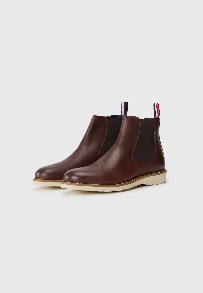 Bottines Chelsea en cuir marron avec des panneaux latéraux élastiques, des bouts arrondis et des semelles en caoutchouc beige. Équipées d'une languette aux couleurs rouge, blanc et bleu.