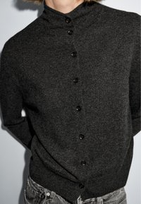Cardigan grigio scuro realizzato in tessuto a maglia, con colletto alto, bottoni frontali e una silhouette aderente con maniche lunghe.