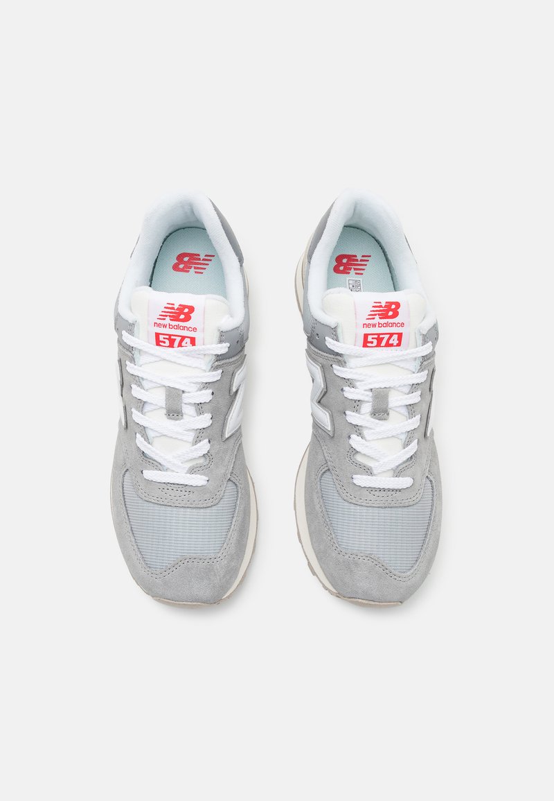Baskets de sport grises avec des matériaux en suède et en maille, dotées de lacets blancs, d'un logo rouge et d'un design à bout arrondi.