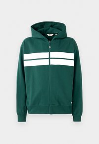 Zeleni zip-up dukserica napravljena od mekog materijala, s podstavljenim kapuljačom i dva bijela horizontalna pruga preko grudi. Riblje manžetne i donji rub.