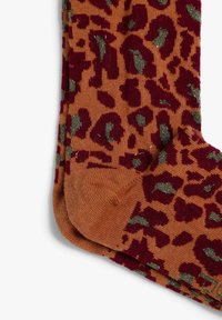 Calcetines naranjas con un patrón de estampado de leopardo en burdeos y acentos metálicos verdes. La textura es suave y de punto, con una puntera reforzada.