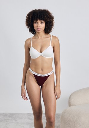 Weißer BH mit Unterdraht und dünnen Trägern, kombiniert mit einem weinroten Slip mit einem weißen Logo-Bund. Glattes Material, minimalistisches Design.