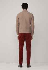 Hnedý pletený sveter s vysokým golierom, doplnený červenými kordovými nohavicami. Oblečenie má textúrovaný povrch a priliehavý strih.