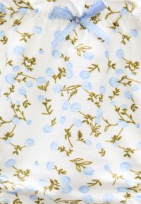 Tissu blanc avec un motif de petites baies bleues et des tiges vertes, orné d'un nœud en satin bleu clair au centre supérieur.