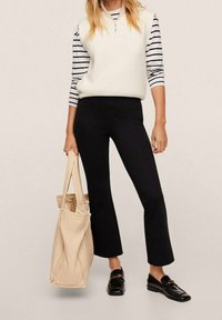 Pantalons évasés noirs associés à un gilet en tricot blanc et une chemise rayée. Un sac tote beige et des slippers noirs complètent l'ensemble. Textures lisses et lignes épurées.