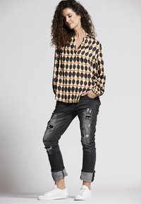 Bluse mit schwarz-orangem kreisförmigem Muster, langen Ärmeln, kombiniert mit zerrissenen schwarzen Jeans und weißen Turnschuhen.