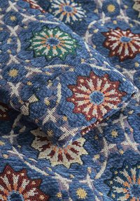 Textilstoff mit blauem Hintergrund und floralen Mustern in Rot, Grün und Weiß, der aufwendige Stiche und Texturen zeigt.
