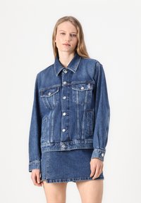 Light denim jacket featuring a button-up front, two chest pockets, and long sleeves. The fabric has a slightly distressed texture and classic fit.