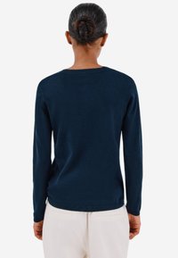 Laivasilmä sininen pitkähihainen neule, jossa on pyöreä pääntie ja ribbireunat. Valmistettu pehmeästä ja sileästä kankaasta, ja siinä on istuva siluetti sekä minimalistinen muotoilu.