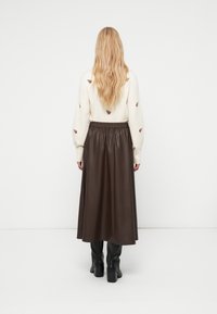 Jupe midi en cuir marron avec une ceinture élastique, associée à un pull crème orné de broderies florales. Des bottes hautes noires viennent compléter la tenue.