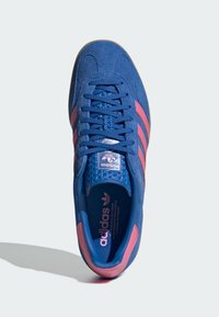 Modré semišové tenisky s ružovými pruhmi, textúrovaným jazykom a logom na päte. Viazací dizajn s polstrovaným interiérom a béžovou podrážkou.