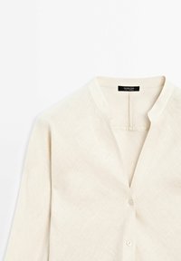 Linned skjorte i lys beige med mandarin-krave, som har en knaplukning og en tekstureret, let krøllet overflade.