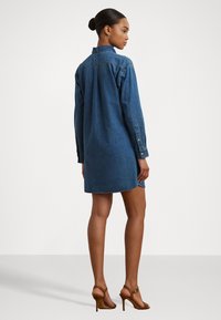 Vestito camicia in denim blu scuro, con maniche lunghe, polsini con bottoni, colletto sagomato e orlo curvo all'altezza della coscia.