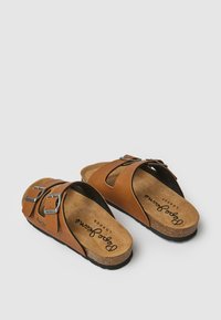 Sandales en cuir marron avec deux sangles réglables en métal à boucle, semelle en liège et semelle noire. Présente un design découpé pour la respirabilité.