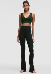 Top sportiv verde închis cu design în formă de V și bretele late, combinat cu colanți evazați verde închis, cu talie înaltă, amândouă din material elastic.
