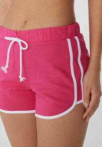 Shorts rose vif avec un cordon blanc et des empiècements blancs sur les côtés. Tissu doux, taille élastique et design ajusté.