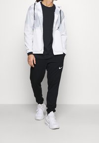 Biała lekka kurtka z szarymi akcentami, czarny T-shirt i czarne dresy. Logo Nikenana spodniach. Na nogach białe sneakersy.