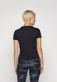 Svart kortermet tettsittende t-skjorte med glatt tekstur og en liten logodetalj på baksiden, sammen med tights med camo-mønster.