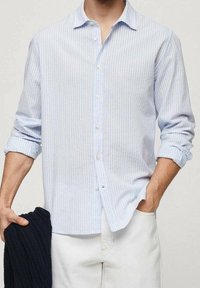 Svetle modrá pruhovaná košile vyrobená z látky s límcem na knoflíky, dlouhými rukávy ohrnutými vzhůru a volným střihem. Doplněná jemnou strukturou.