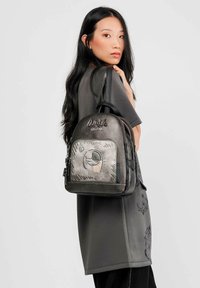 Mochila negra de cuero con detalles en gris, que presenta un diseño gráfico, cierre de cremallera y correas ajustables. Logo bordado en la parte delantera.