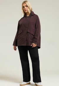 Veste à capuche bordeaux avec fermeture à boutons, deux poches avant et une coupe décontractée. Associée à un pantalon noir à jambes droites et des baskets blanches.