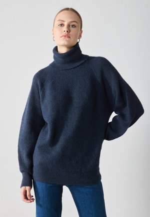 Mørk marineblå oversized turtleneck genser laget av teksturert strikkemateriale, med lange ermer og en avslappet passform. Brukt med blå jeans.