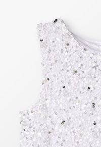 Witte mouwloze top bedekt met glanzende witte en zilveren pailletten; gladde textuur met afgeronde halslijn en gestikte zoom.