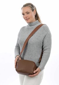 Borsa a tracolla in pelle marrone con superficie texturizzata, design imbottito e dettagli in metallo argentato, indossata sopra un maglione grigio.