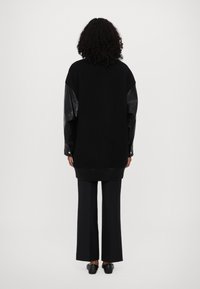Czarna, oversize bluza z krojem o dużych rękawach wykonanych ze skóry, z prążkowanymi ściągaczami na rękawach i na dole. Noszona z szerokimi czarnymi spodniami i prostymi czarnymi butami.
