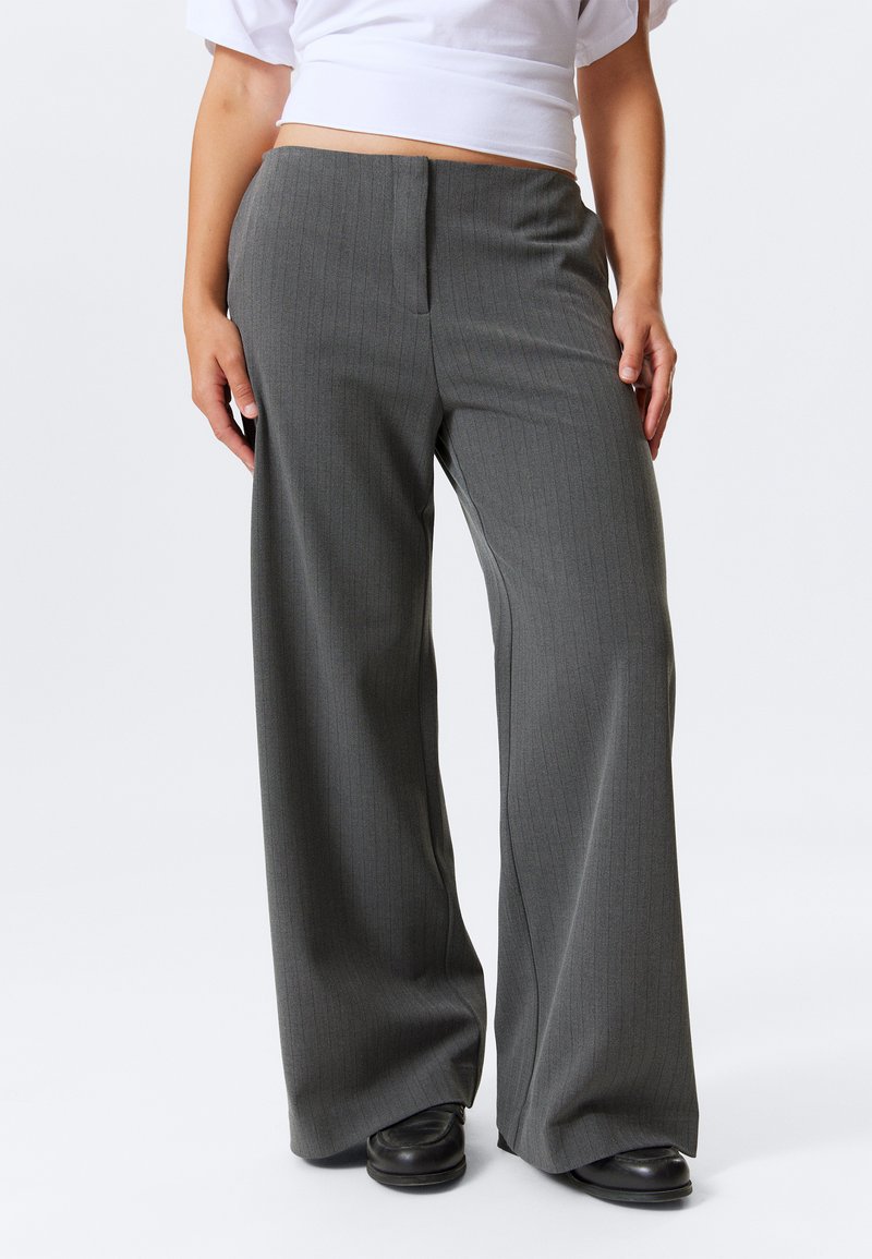 Pantalons gris à rayures fines avec une coupe large, présentant un devant plat et une texture lisse, associés à des chaussures noires.