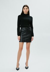 Maglione nero a maglia con texture a coste, abbinato a una gonna a tubino in pelle nera a vita alta con zip frontale. Tacchi a punta neri.