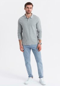 Ljusgrå långärmad polo med krage, i kombination med ljusblå denimjeans och vita sneakers. Enkelt, avslappnat design.