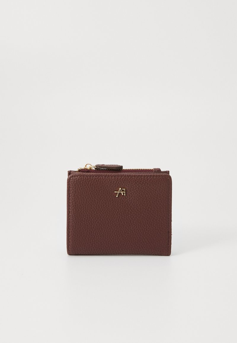 Portefeuille en cuir bordeaux avec une surface texturée, arborant un logo doré et une fermeture éclair. Forme rectangulaire compacte.