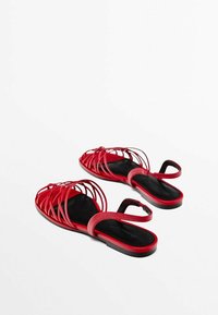 Sandales plates rouges avec des brides croisées ouvertes, une semelle plate et une bride arrière. Texture en cuir lisse avec une semelle intérieure noire et un design minimaliste.