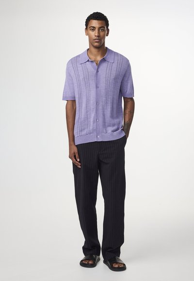 Lavendel kortef mouw knoop-overhemd met gestructureerde verticale strepen, gecombineerd met zwarte broek met streepjes en zwarte slip-on sandalen.